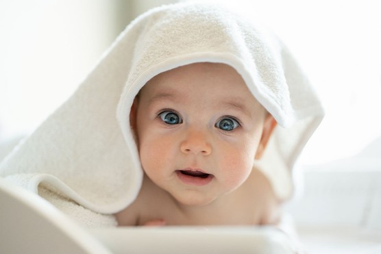 Baby looking straight at camera with big blue eyes and wearing a towel on head