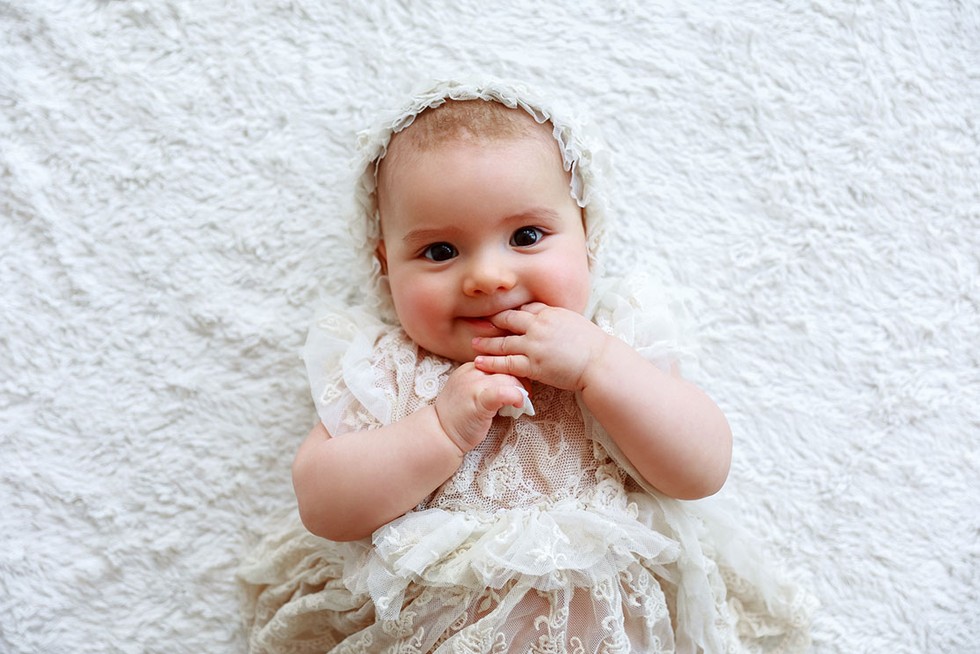baby girl lying down wearing an old fashioned dress and bonnet