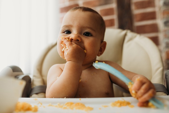 baby in high chair feeding itself while weaning