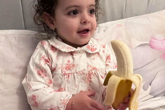 toddler sitting in bed eating a banana