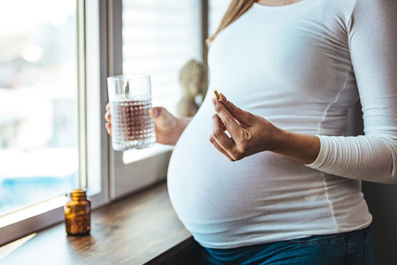 Close up of a pregnant woman's bump with a supplement in her hand and glass of water