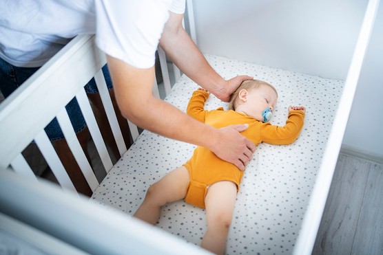 father putting baby into cot to sleep