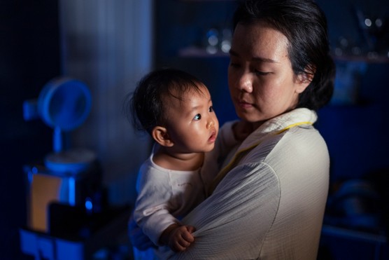 Mother with her eyes closed holding a very awake baby.