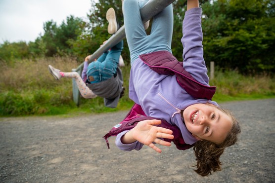 Close-up shot of young triplets playing in the North East of England. They are wearing warm clothing and looking at the camera while hanging upside down on a metal bar.