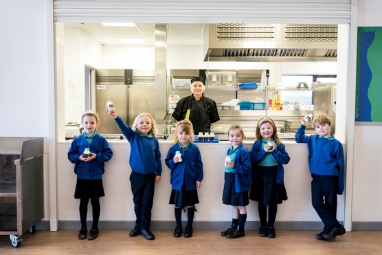 Lunch hall portrait of school cook and children with milk