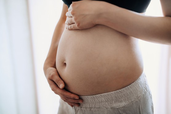 Close-up, mid-section of pregnant woman gently touching her small baby bump.