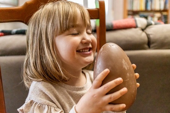 Portrait of a happy little blonde girl with her eyes closed holding a chocolate Easter egg at home.