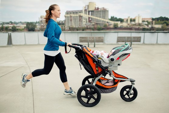 Side view of woman pushing baby stroller while jogging in city