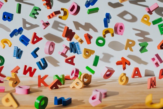 Conceptual image of colourful falling letters, casting shadows on a white wall.