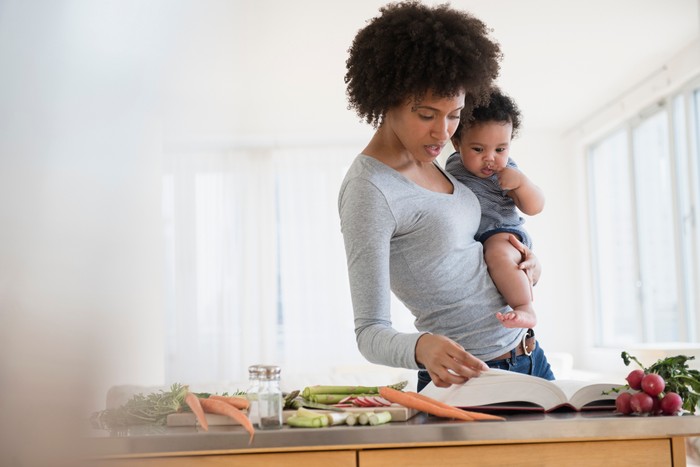 Mother reading cookbook while holding baby son Mother reading cookbook while holding baby son
