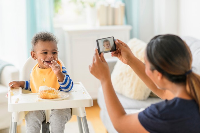Mixed race mother photographing messy baby boy in high chair