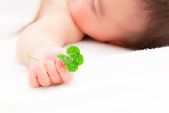 baby lying down with arm outstretched holding a four-leafed clover or shamrock
