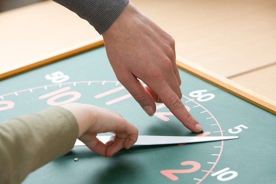 close up of child and teachers hands learning to tell the time on analogue clock