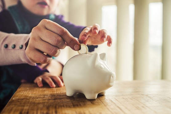 Mother and her little daughter puting in savings into a white piggy bank.