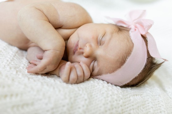 newborn baby girl with pink bow on head lying asleep on blanket