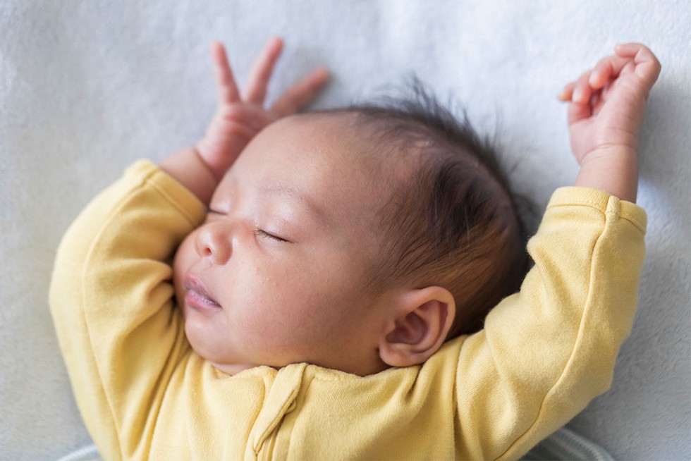 baby boy in yellow sleep suit, asleep with arms up