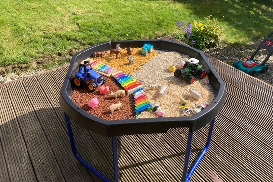 a tuff tray for children set up in a garden with farm small world activity