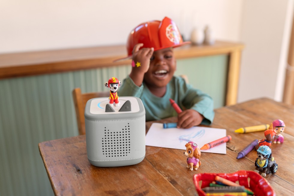 A child wearing a Paw Patrol hat laughing while drawing and listening to Paw Patrol on Toniebox 2