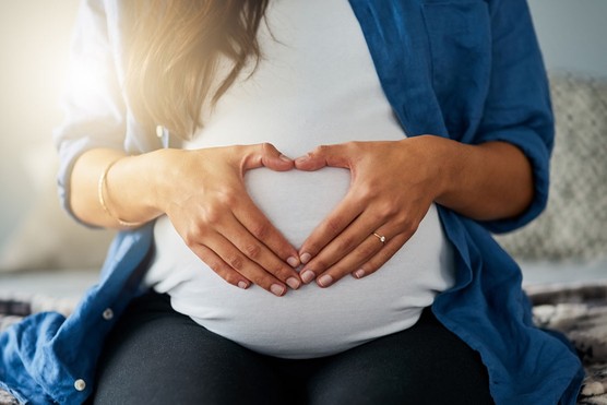 close up of a pregnant woman holding her hands in a heart shape over her bump