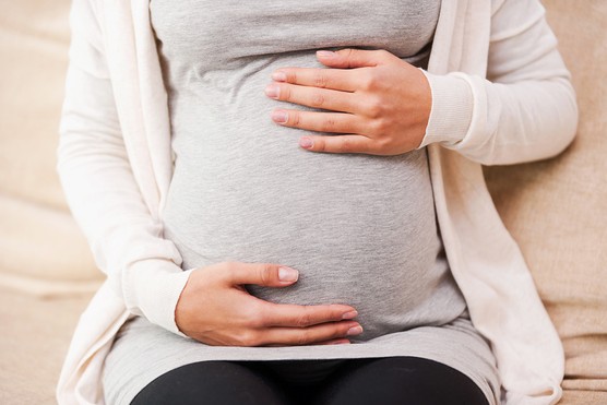 Close-up of young pregnant woman touching her abdomen while sitting on the couch